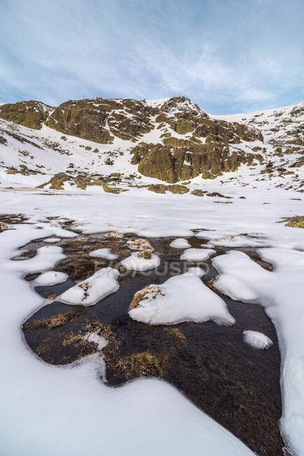 Paesaggio di pendio innevato di collina in altopiano sotto cielo nuvoloso alla luce del giorno e un fiume di acqua ghiacciata — Foto stock
