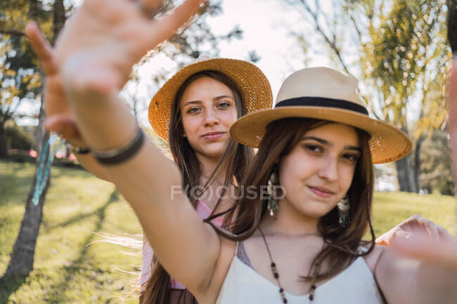 Content female teenagers with outstretched arms interacting while looking at camera on meadow in summer — Stock Photo
