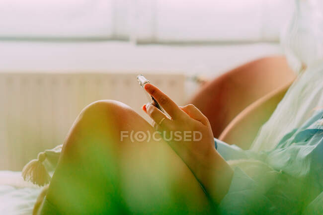 Side view of crop female in shirt surfing internet on mobile phone while sitting in light room — Stock Photo