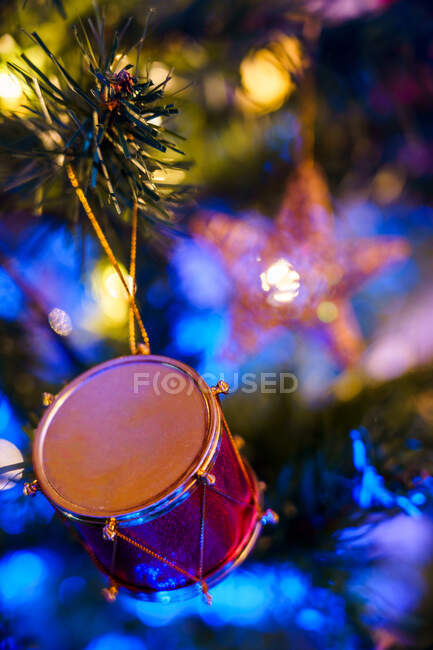 Декоративные игрушки в форме барабана, висящие на ветвях хвойной елки с блестящей гирляндой — стоковое фото