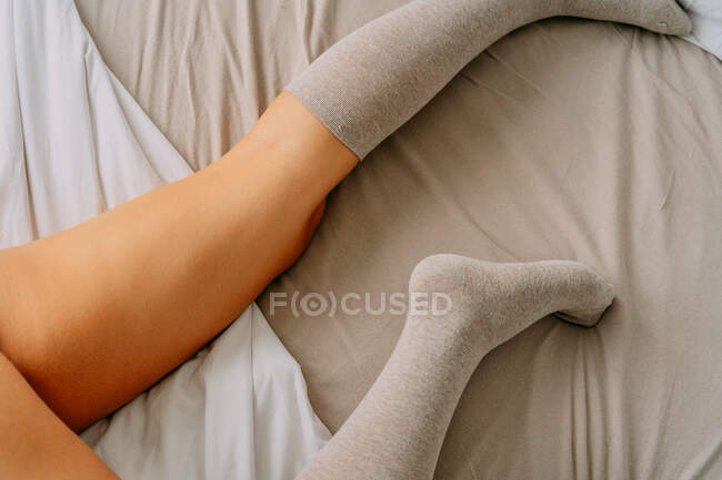 Colheita fêmea irreconhecível em meias de joelho deitado em lençol amassado — Fotografia de Stock