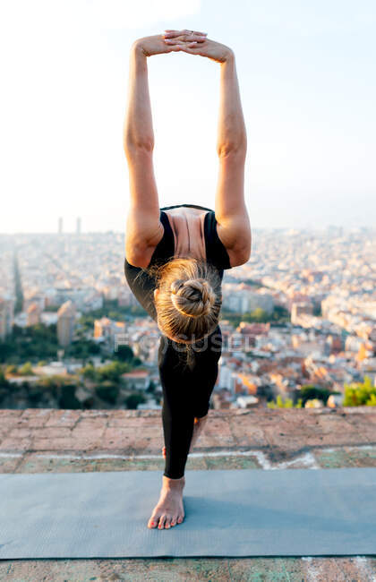 Femme flexible méconnaissable posant Garudasana tout en se penchant vers l'avant avec les bras levés pendant la pratique du yoga contre les bâtiments urbains — Photo de stock