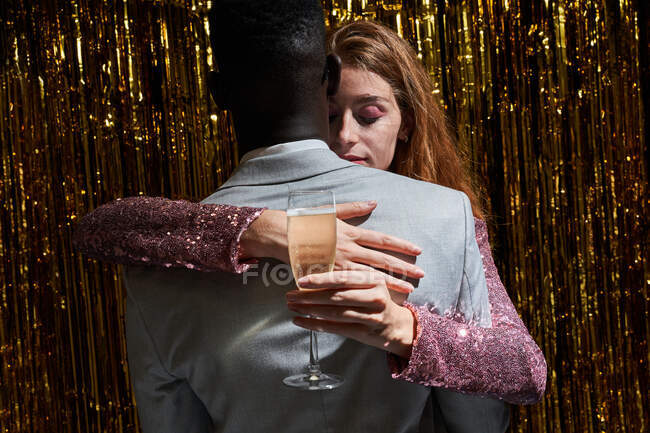 Стильная многонациональная пара с бокалом шампанского обнимает ее с анонимным черным парнем во время празднования Нового года — стоковое фото