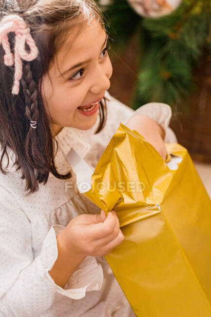 Criança sorridente abrindo caixa presente durante o feriado de Ano Novo em casa — Fotografia de Stock