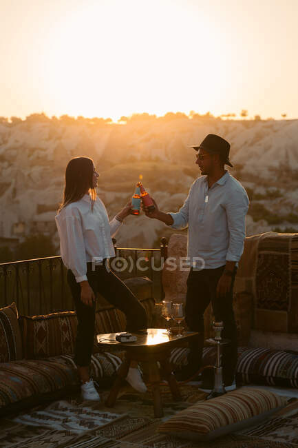 Side view of couple with beer looking at each other while spending time on balcony at sunset in Cappadocia, Turkey — Stock Photo