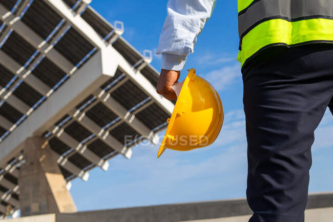 Low angle back view of crop unrecognizable male inspector in vest with protective helmet against modern solar power station — Stock Photo