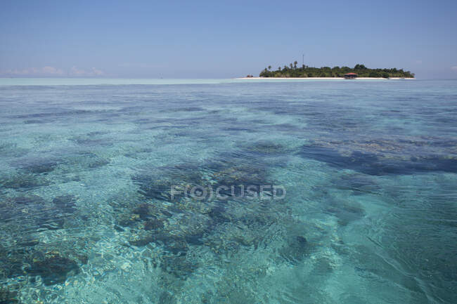 Прозрачная волнистая вода бесконечного моря с песчаным дном и островом под голубым небом в Малайзии — стоковое фото
