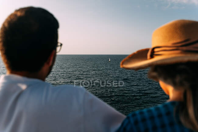 Vista posterior de una pareja anónima de turistas contemplando el mar y el barco bajo un cielo azul claro en Saint Jean de Luz - foto de stock