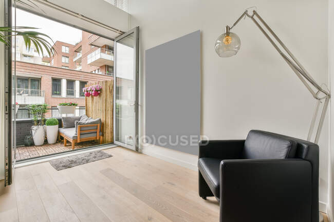 Moderno soggiorno interno con divano in pelle e lampada da terra contro piante in vaso sul balcone durante il giorno — Foto stock