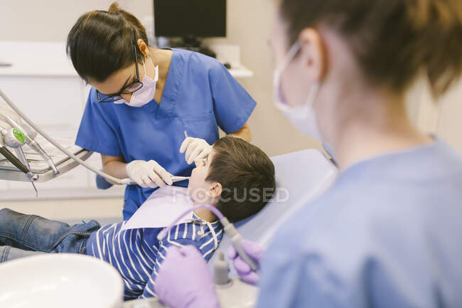 Ângulo alto do dentista e assistente que trata dentes do menino durante o procedimento na clínica de odontologia — Fotografia de Stock