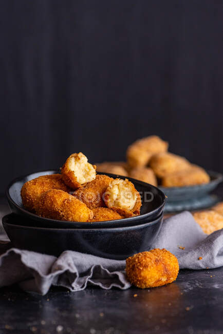 Tasty croquettes with cheese filling and golden crust in bowl on towel on dark background — Stock Photo
