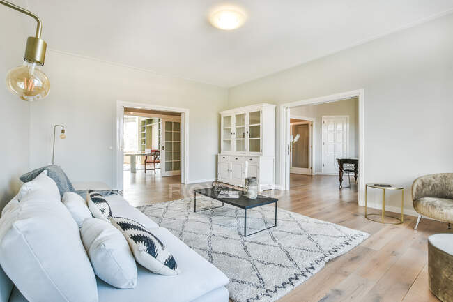 Weiche Couch mit Kissen in der Nähe des Tisches auf Teppich im geräumigen hellen Wohnzimmer mit Sessel — Stockfoto