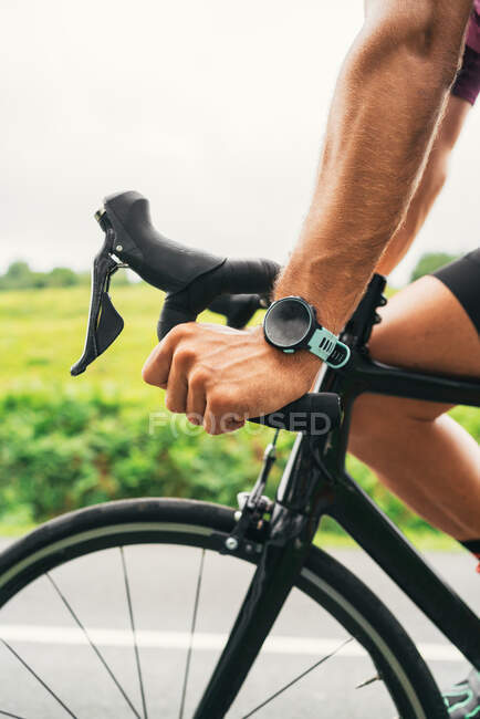 Vista lateral da cultura desportista irreconhecível no rastreador wearable andar de bicicleta moderna durante o treinamento na estrada no campo — Fotografia de Stock