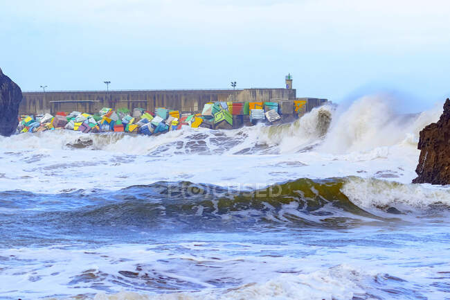 Мощные морские волны, плескающиеся над волнорезом с красочными кубами памяти, расположенными в порту Льянес в Астурии, Испания — стоковое фото