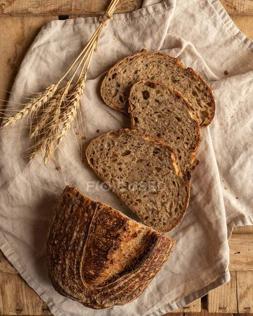Вид сверху свежих кусочков хлеба с пшеничными пряностями на складной ткани на деревянной поверхности — стоковое фото