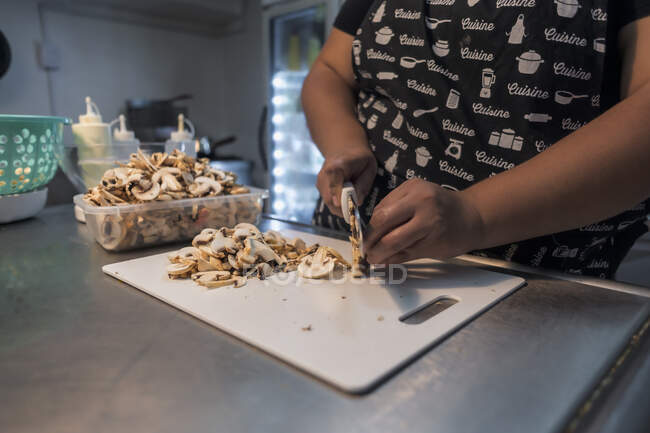 Cropped unrecognizable woman cutting raw mushrooms on chopping board at work in restaurant — Stock Photo