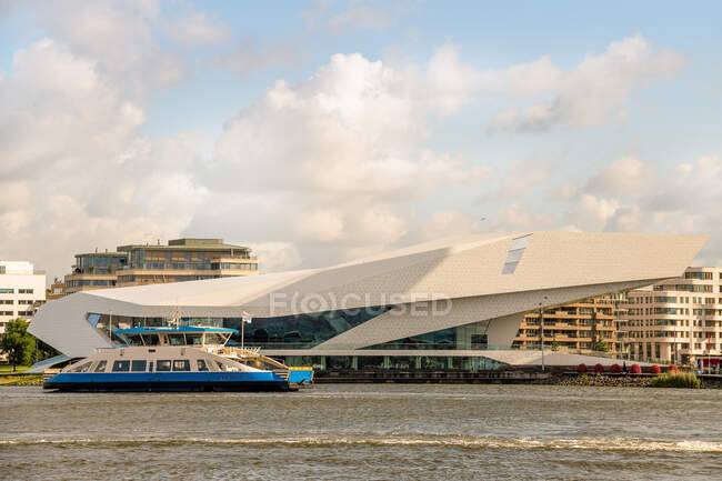 Boot schwimmt auf plätscherndem Fluss am EYE Film Institute Netherlands vorbei, das sich an der Küste in Amsterdam befindet — Stockfoto