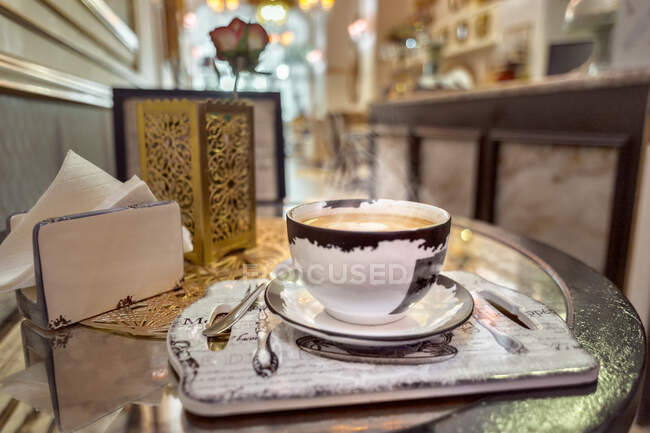 Taza de cerámica de café aromático con latte arte en la mesa con servilletas y rosa en flor en la cafetería - foto de stock
