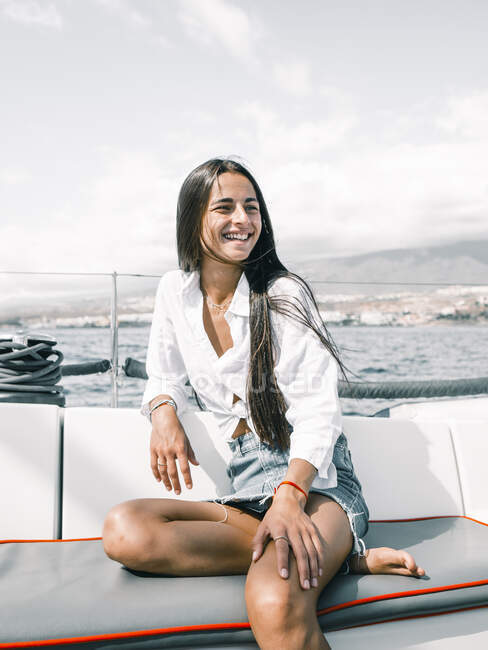 Созерцательная счастливая девушка-подросток, сидящая со скрещенными ногами на скамейке моторной лодки в океане, глядя в сторону на Тенерифе, Испания — стоковое фото