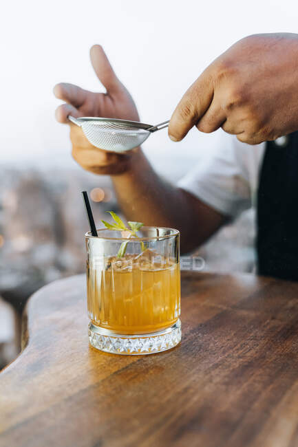 Анонимный бармен просеивает порошок, чтобы виски разбил коктейль кубиками льда на прилавке — стоковое фото