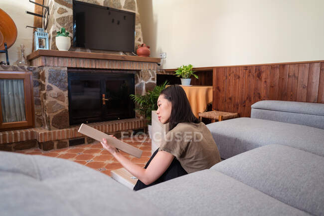 Jovem atencioso étnico feminino montando mesa no tapete ornamental contra sofá na sala da casa de luz — Fotografia de Stock