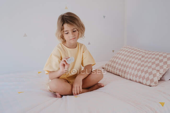 Barefoot child in t shirt with pacifier sitting with crossed legs on soft bed in house — Stock Photo