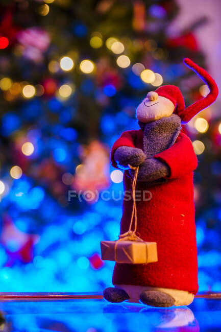 Gnomo giocattolo morbido per la celebrazione del Natale posto sul tavolo contro l'albero di festa sfocato decorato con ghirlande incandescenti — Foto stock
