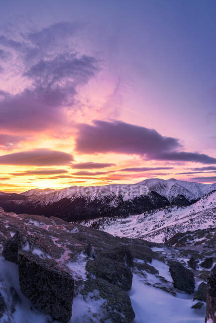 Pintoresco paisaje de montañas rocosas cubiertas de nieve bajo el colorido cielo nublado al amanecer - foto de stock