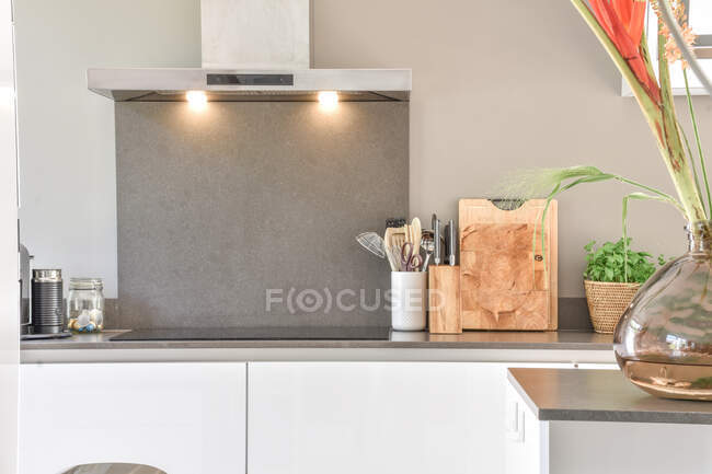 Tabla de cortar de madera y utensilios de cocina colocados cerca de la estufa en el mostrador de cocina en apartamento moderno - foto de stock