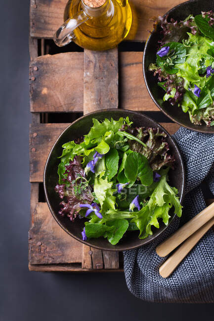 From above of tasty vegetarian salad with green and red lettuce leaves and edible flowers against jug of oil — Stock Photo
