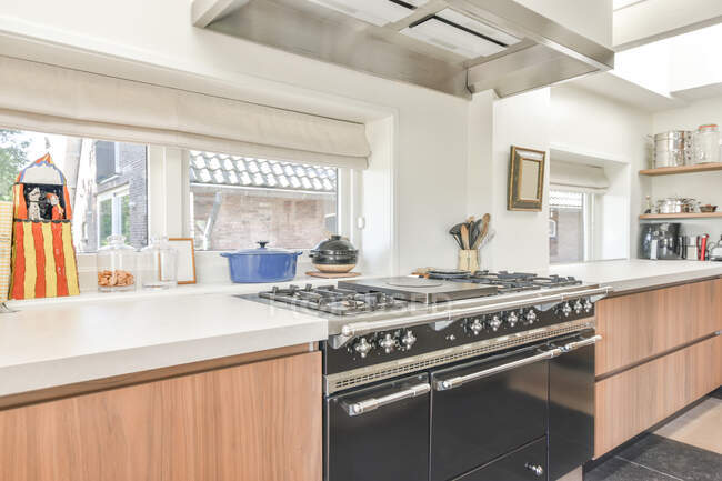 Diseño creativo de cocina con estufas eléctricas y de gas entre mesas con utensilios de cocina en casa de luz - foto de stock