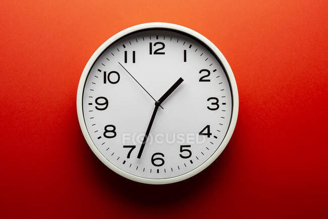 Reloj minimalista en forma redonda con números y flechas sobre fondo rojo colorido - foto de stock