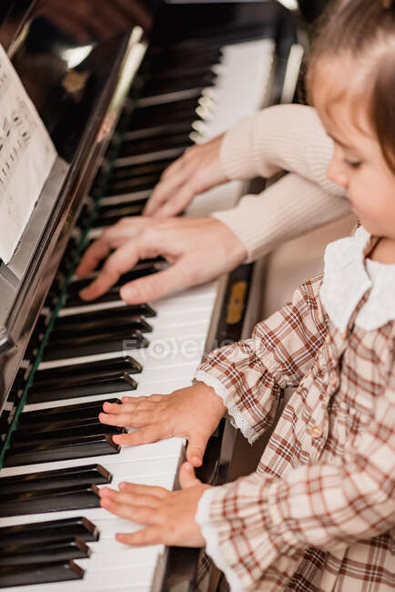 Ernte unkenntlich Kind im karierten Kleid spielt Klavier, während die Freizeit zu Hause auf verschwommenem Hintergrund — Stockfoto