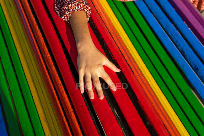 Сверху анонимная женщина трогает спинку красочной скамейки в солнечный летний день в парке — стоковое фото