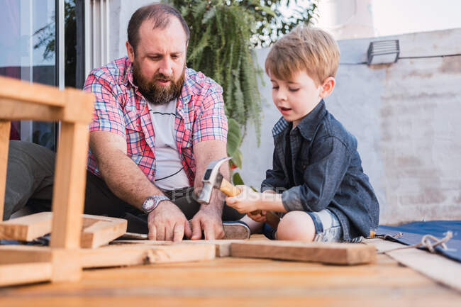 Bärtiger Papa lehrt Sohn am Wochenende mit Hammer Holzarbeiten auf der Promenade — Stockfoto