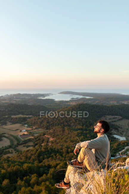 Männliche Reisende bewundern Meer und Plantagen mit Bäumen, während sie sich bei Sonnenuntergang auf dem Kamm ausruhen — Stockfoto