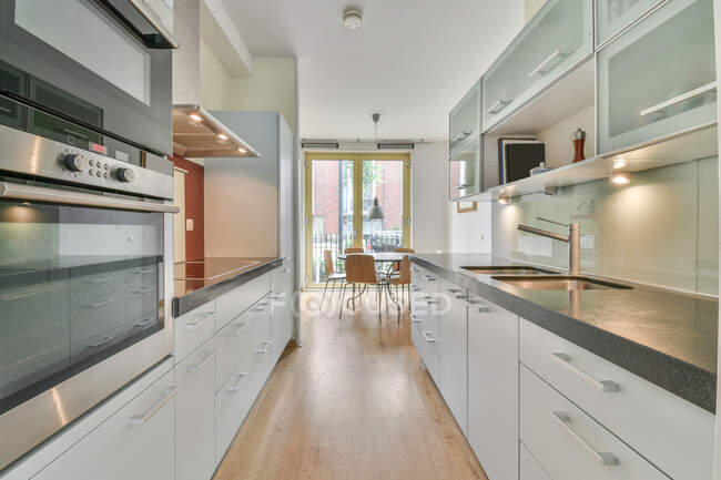 Interior of kitchen with built in appliances and white cabinets with dining table and chairs — Stock Photo