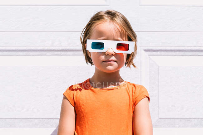 Linda chica en ropa colorida casual y gafas tridimensionales de pie sobre fondo de pared blanca mirando a la cámara - foto de stock