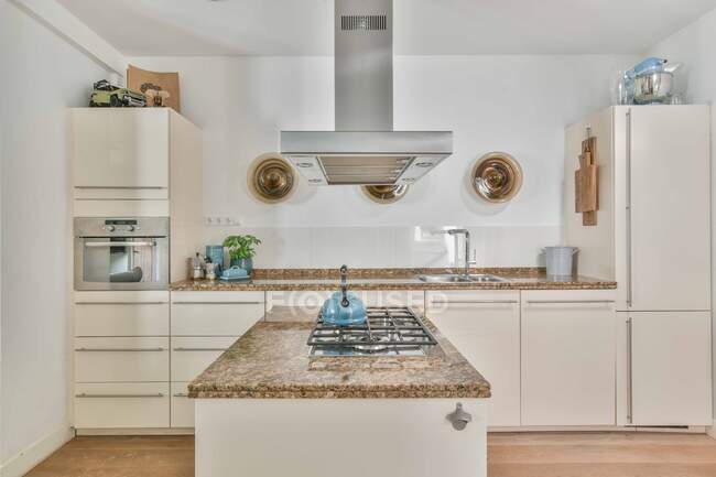 Bouilloire placée sur la cuisinière sous ventilation dans une cuisine spacieuse avec des meubles légers dans un appartement moderne — Photo de stock