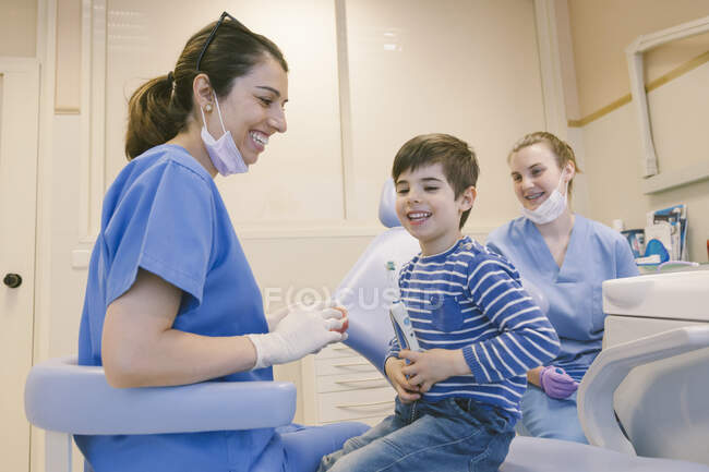Sorridente ortodontista femminile che insegna al paziente con lo spazzolino da denti a lavarsi i denti sul modello della mascella in clinica dentale — Foto stock
