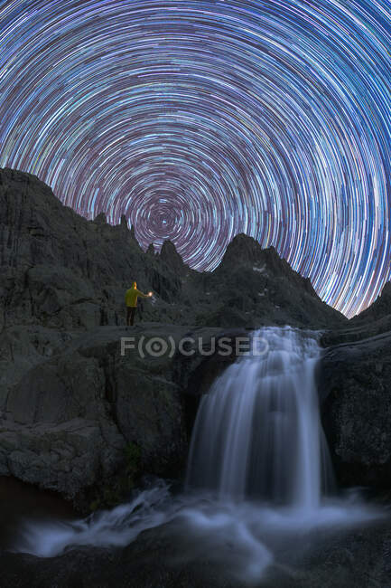 Мандрівник захоплюється каскадом з піною на шорсткій гонці проти ставка під рухомим зоряним небом в сутінках — стокове фото