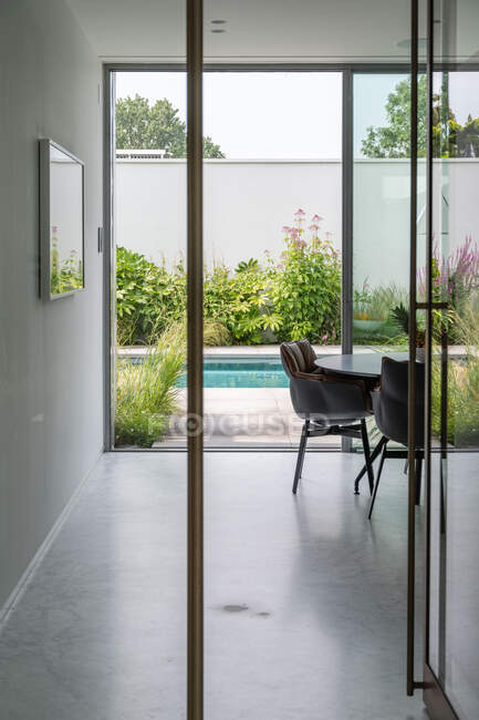 Vazio corredor espaçoso de villa residencial moderna que leva ao quintal com piscina e plantas verdes no dia ensolarado — Fotografia de Stock