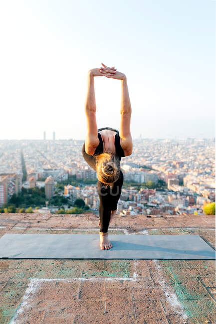 Unrecognizable flexible female performing Garudasana pose while leaning forward with raised arms during yoga practice against urban buildings — Stock Photo