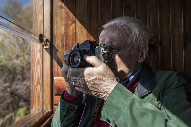 Homme prenant des photos avec son vieil appareil photo par la fenêtre d'une vieille voiture de train en bois — Photo de stock