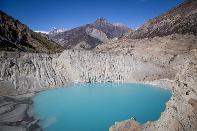 Paisaje de lago azul rodeado de montañas rocosas con pendientes pronunciadas en el vasto valle de Nepal - foto de stock