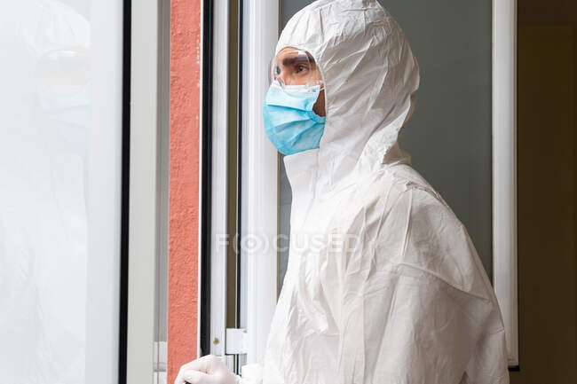 Вид сбоку вдумчивого взрослого мужчины-медика в индивидуальном защитном оборудовании, дышащего свежим воздухом в больнице — стоковое фото