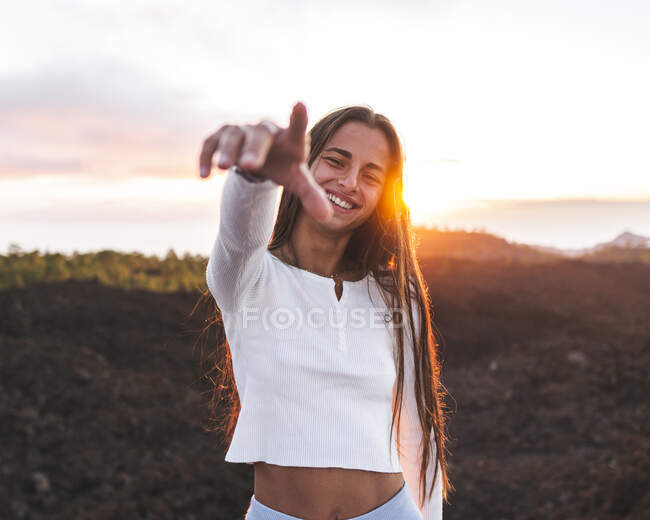Zufriedene Teenagerin mit ausgestrecktem Arm, die bei Sonnenuntergang auf Teneriffa in die Kamera schaut — Stockfoto