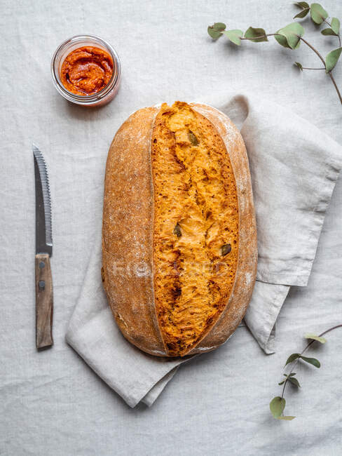 Draufsicht auf frisch gebackenes Brot mit roter Pesto-Sauce im Glasgefäß, serviert auf dem Tisch mit Serviette und Messer — Stockfoto