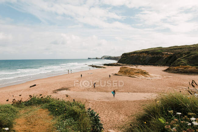 Travelers on sandy coast against mount and foamy ocean with horizon under cloudy sky in Cantabria Spain — Stock Photo
