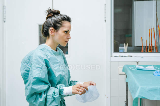 Junge Tierärztin in grüner Uniform setzt Einmalmütze auf und freut sich auf Klinik — Stockfoto